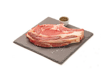 chuletón de ternera fresco crudo con pimienta verde cruda y sal gorda decorativa sobre un plato de pizarra negro. aislada fondo blanco