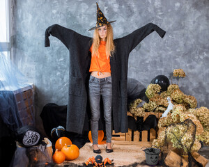 Teenage girl among the decor for Halloween holiday, in huge jacket in role of ghost