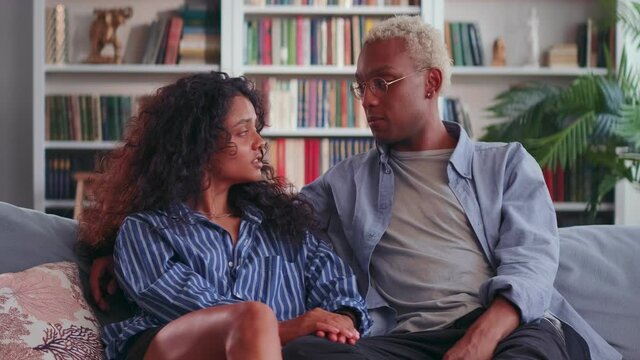 Happy mixed race couple relax on couch talking enjoy spending time together at home. Smiling African husband and Indian wife sit on sofa chatting and laughing holding hands. Relationship goals concept