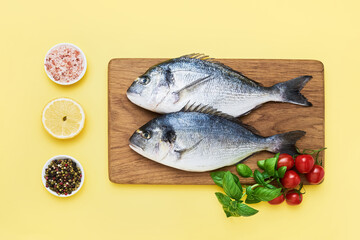 Dorado fish with spices on a wooden cutting board on a light yellow background. Mediterranean seafood concept. Top view, copy space