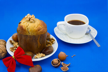 Panettone decorated with dried fruits next to a cup of coffee on a blue background