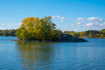 Fototapeta premium View of a small rocky island with the deciduous trees in vibrant autumn colors.