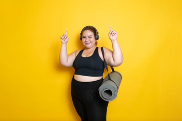 sporty plus size woman with yoga mat pointing up, weight loss concept