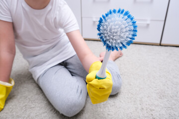 A child in yellow rubber gloves showing bruses for cleaning house, carpet from dust and stains