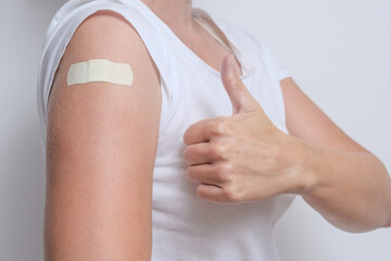 A woman showing thimb up and her arm with an adhesive bandage after injection of vaccine. Happy of getting vaccinated from corona virus, covid-19