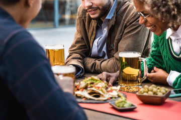Happy multiracial people having fun during brunch meal time at brewery bar - Focus on center man