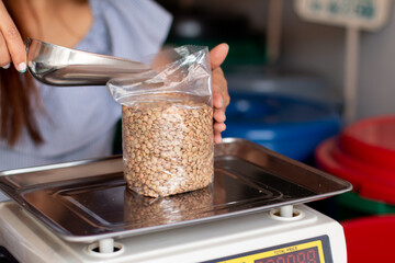 Woman packing lentils in bag and using scale. Woman using metal spoon to pack grains. Dry grain store.