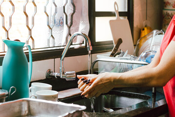 In this photo illustration a woman washes her hands in the sink full of dirty dishes.