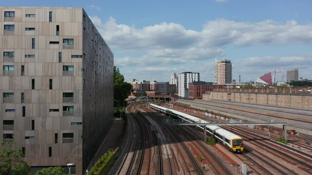 Forward tracking of passenger train driving on multi track railway line leading around modern designed apartment house. London, UK