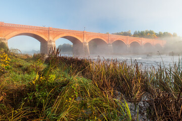 Long red brick bridge in foggy, sunny morning, Kuldiga, Latvia.