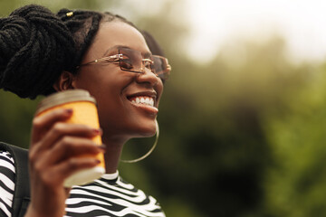 african young woman, wearing sunglasses, holds coffee in takeaway glass