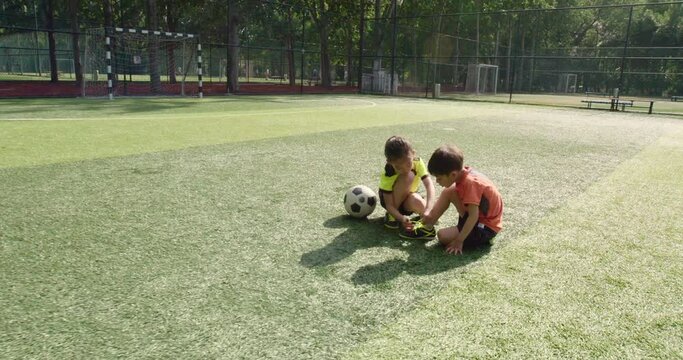 Little girl helping her brother to tie shoelace on soccer field,4K