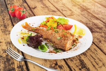 Tasty fish dish in a bowl, fork on a wooden table. Low calories healthy eating