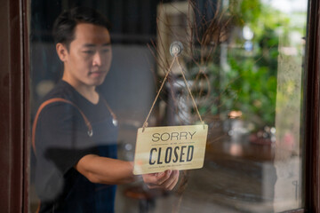 Asian man coffee shop barista walking to cafe door and turning hanging closed sign to open. Male...