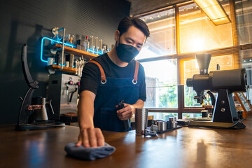 Asian man barista using towel sweeping counter bar with alcohol sanitizer before opening cafe. Male...