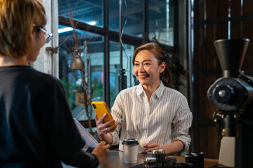 Fototapeta na wymiar Asian woman customer using smartphone scanning bar code make contactless payment to barsita at cashier counter in coffee shop. Small business with modern mobile banking electronic payment concept
