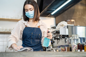 Cafe waiter wear mask, clean restaurant with sanitizer to open store.