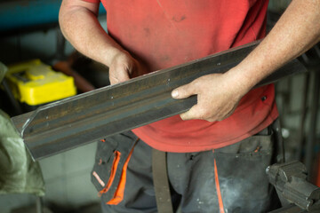 Worker with metal. The guy holds a steel part. Hard work in a metalworking workshop. Creation of steel construction.