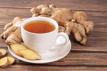 Fresh ginger tea in cup with ginger root and sliced on wooden table.