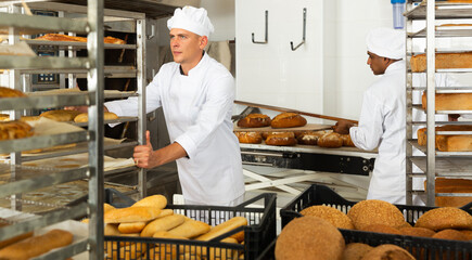 male baker with bread in baking shovel and cart in kitchen
