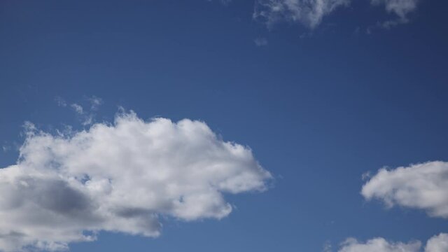 Fast moving white fluffy clouds on a blue sky. Time-lapse of fast approaching cumulus clouds.