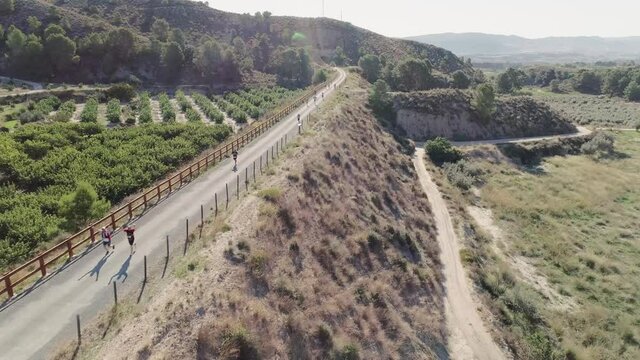 Runners Running On Countryside Road On A Sunny Summer Day In Murcia, Spain. - aerial