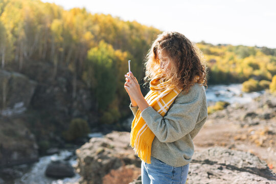 Young beautiful woman with curly hair taking photo on mobile phone on magic view background of mountains and river, hiking on autumn nature