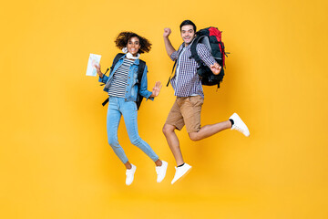 Happy young interracial tourist couple with backpacks ready to travel jumping in yellow color...