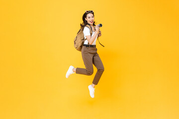 Fototapeta na wymiar Young pretty Asian woman tourist backpacker smiling and jumping with camera in hand isolated on yellow studio background
