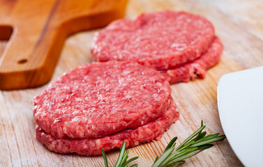 Fresh raw minced beef patties for hamburgers on wooden surface with herbs