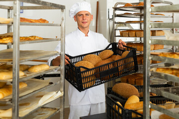 Positive man worker of bakery carrying box of bread standing at kitchen