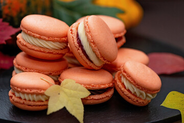 Dessert for Halloween. Thanksgiving menu. French pastry macarons. Macaroons with chocolate and mascarpone on a black stone board with pumpkins and autumn leaves. Soft selective focus. Close-up