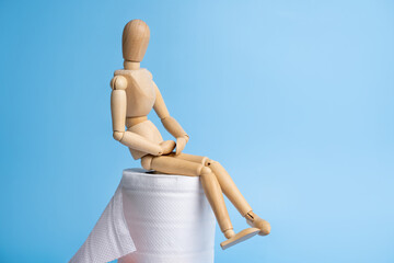 Wooden figure sit on a roll of toilet paper. Concept of the problem with digestion.