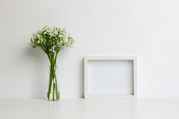 A white photo frame with flowers over the light wall. 
