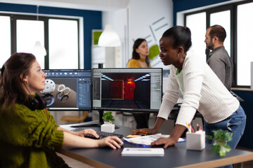 Multiethnic women designer looking at computer with dual displays working together at gaming project in company office. Gamer workers developing new games application on pc with modern technology © DC Studio