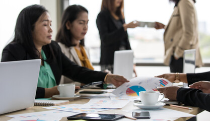 Close up shot of white hot coffee cup and dish on working meeting desk while unidentified unrecognizable businesswoman in casual business clothing working and cheers celebrating in blurred background