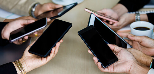 Unidentified unrecognizable businesspeople holding showing black blank digital touchscreen tablet and smartphone gadgets with copy space text together around work table in meeting room company office