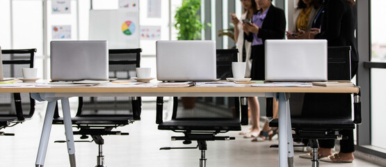 Unidentified unrecognizable female officer staffs taking break standing chatting using smartphone at office workspace with laptop notebook computer paperwork documents coffee cups on working table