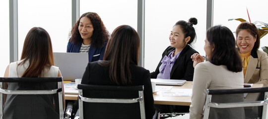 Group of Asian mature adulg female businesswoman officer staffs in formal suit sitting smiling look at big monitor screen greeting say hello to multicultural colleagues on teleconference