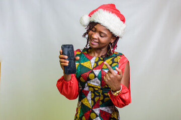 An african lady from Nigeria pointing to the smart phone in her hands and also wearing a christmas...