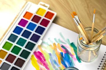 Obraz premium watercolor paints and a jar with brushes on an album sheet with samples of paints