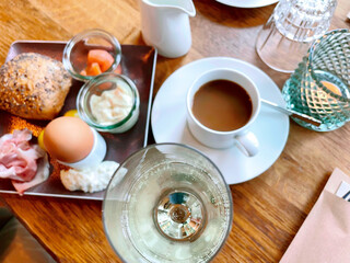Table laid for breakfast outside in summer with various jams, bread, coffee, croissants, eggs, bacon muesli and orange juice