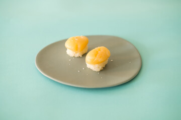 Two Nigiri Sushi with scallop served on light grey plate. Two sushi pieces served on the plate isolated on turquoise background. Japanese food. 