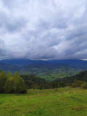 Carpathian landscape with cloudy sky. A green meadow in mountains near old forest. Lifestyle in the Carpathian village. Ecology protection concept. Explore the beauty of the world.