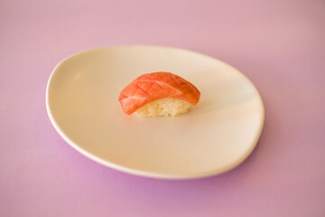 Sushi Nigiri with raw tuna served on white plate. One sushi piece on the white plate isolated on pink background. Japanese traditional food. 