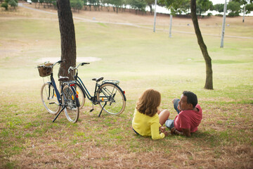 Happy mature couple resting with bikes in park. Senior man and woman lying on grass and talking. Mature love and active seniors concept