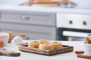 Board with uncooked cinnamon rolls on table in kitchen