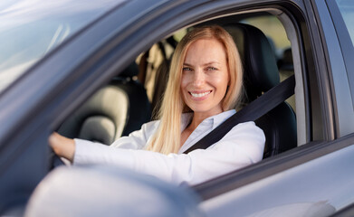 Portrait of smiling mature lady in formal wear sitting inside luxury car and keeping hands on...
