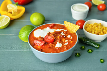 Bowl with tasty chili con carne and ingredients on table