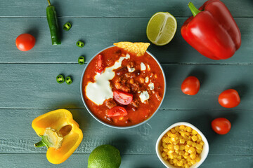 Bowl with tasty chili con carne and ingredients on color wooden background